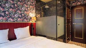 A hotel room with a bed, a shower, and a door with a golden frame. - The Place Brussels (Brussels)