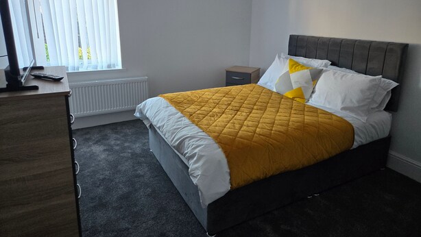 A bedroom with a bed, a bedside table, a desk, and a window with blinds. - Room-cozy Guest Rooms in Bedford With Sh (Bedford)