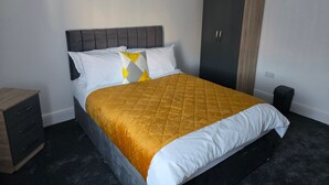 A bed with a quilted headboard, a wardrobe, a bedside table, and a trash bin. - Room-cozy Guest Rooms in Bedford With Sh (Bedford)