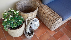 Wicker meubels, een potplant en een lantaarn op een betegelde vloer.