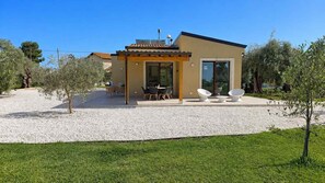 Ein modernes Haus mit Terrasse, Sitzgelegenheiten im Freien und einem Schotterweg.