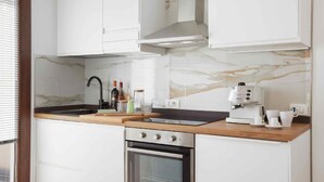Een moderne keuken met witte kasten, een marmeren achterwand, een ingebouwde oven en een koffiezetapparaat.
