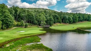 Ein Golfplatz mit Teich, umgeben von dichtem Wald und einer Brücke.