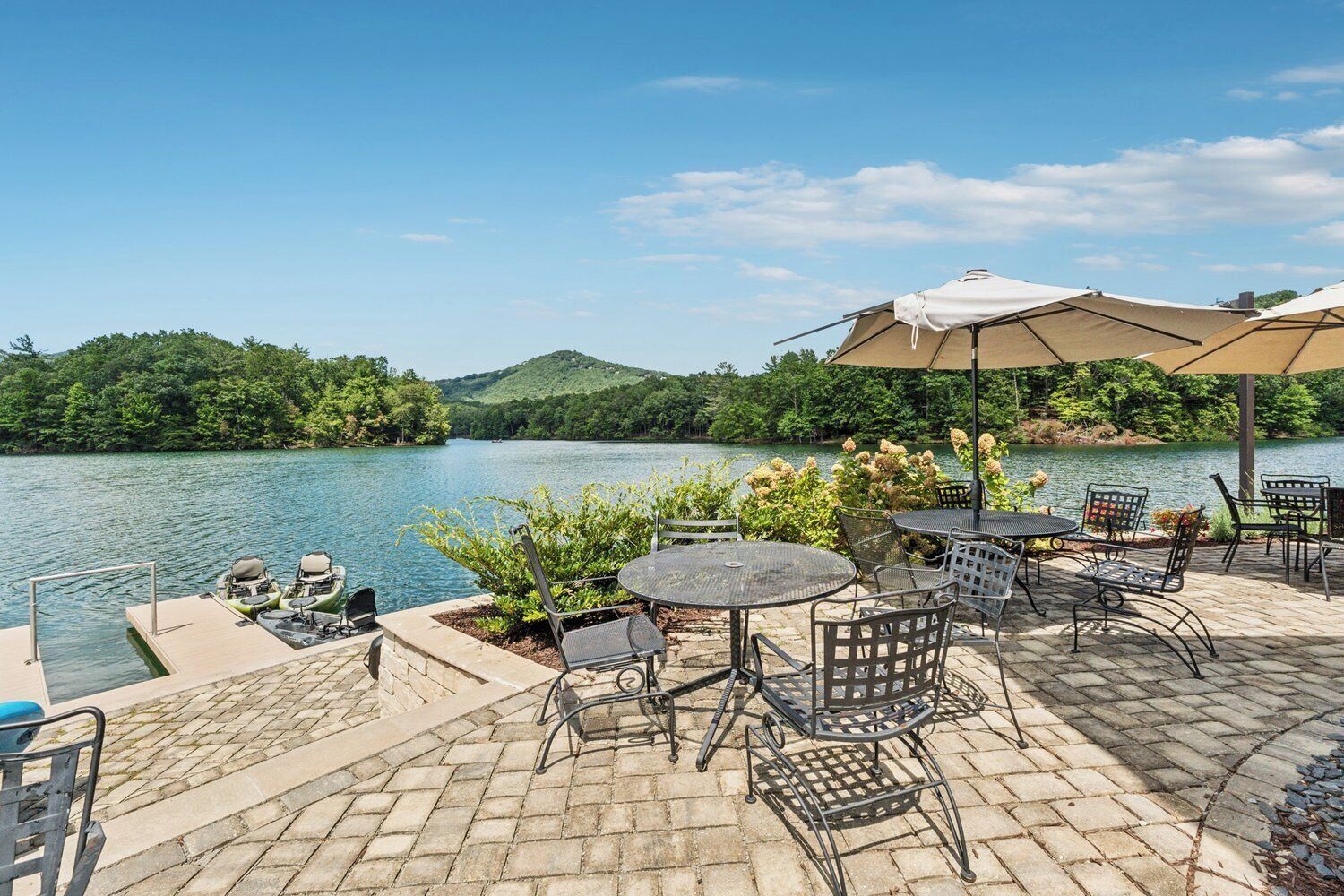 Eine Terrasse mit Sitzgelegenheiten im Freien, ein Steg mit Booten und Blick auf einen See.