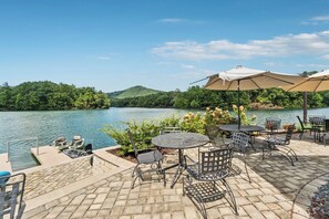 Eine Terrasse mit Sitzgelegenheiten im Freien, ein Steg mit Booten und Blick auf einen See.
