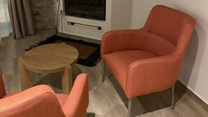 A modern living room with a stone accent wall, a flat-screen TV, and two orange chairs. - Miltilon (Xylokastro-Evrostina)