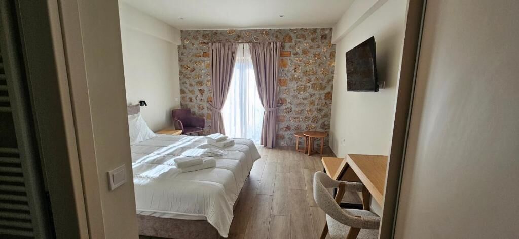 A bedroom with a bed, a chair, a small table, and a window with curtains.