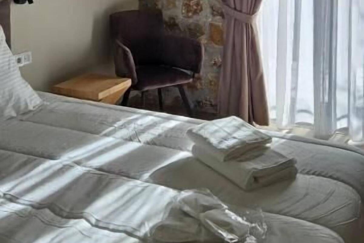 Habitación de hotel con cama, una silla, una mesita y pared con diseño de piedra.
