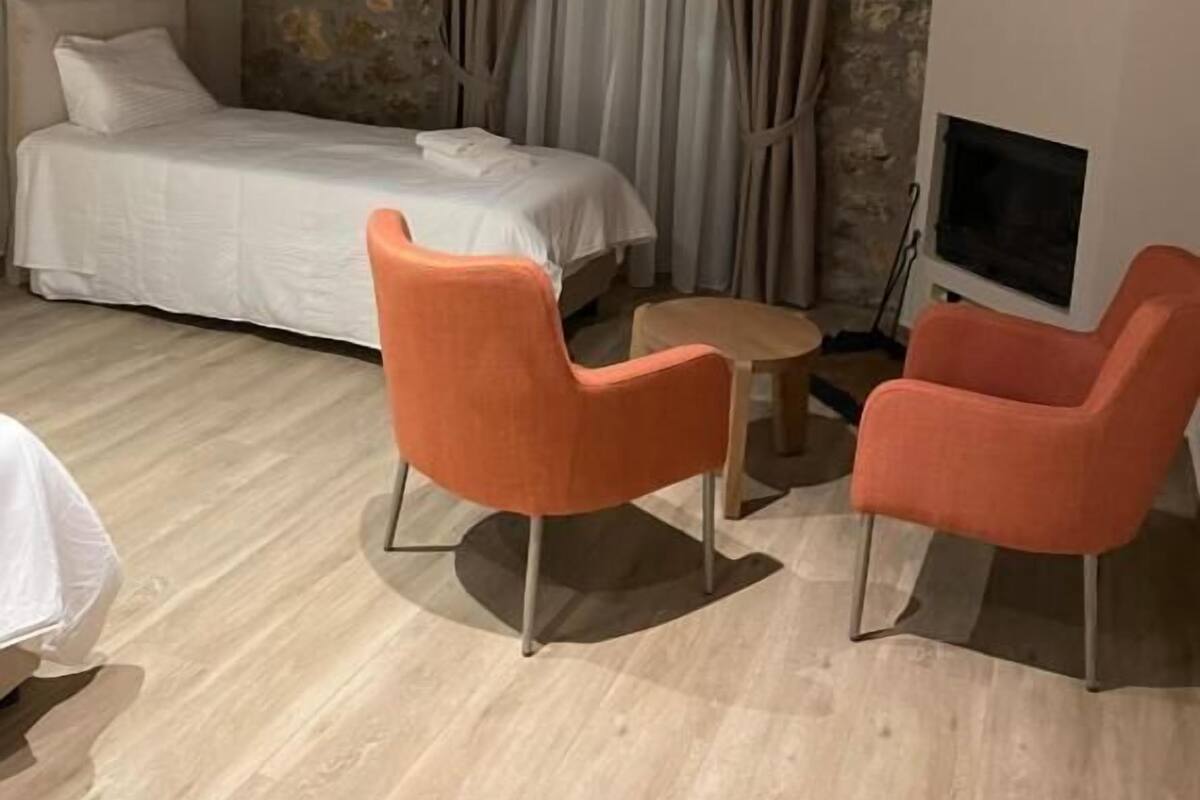 Un dormitorio con una cama, dos sillones anaranjados, una mesita, un televisor y paredes de piedra.