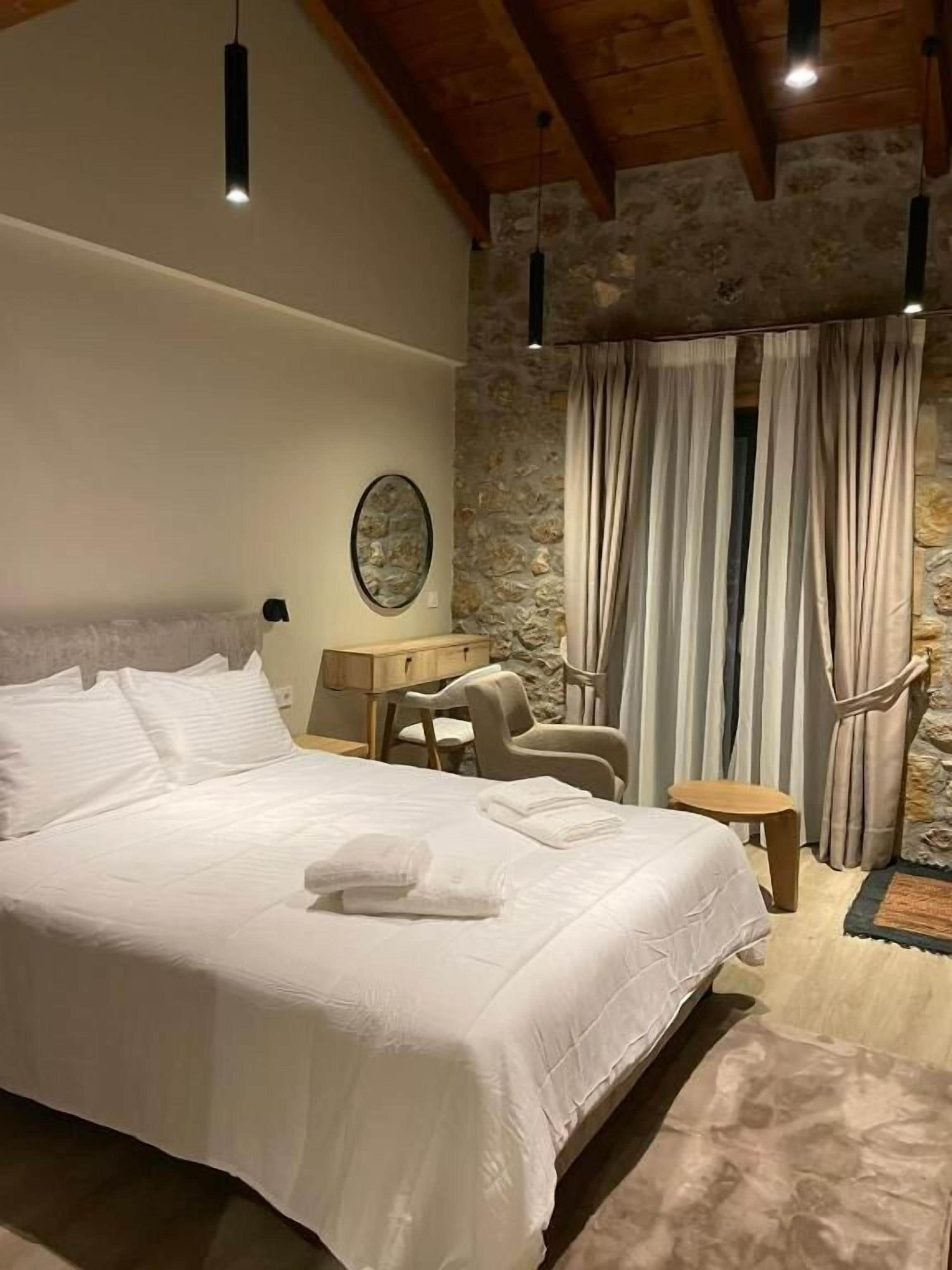 Een slaapkamer met een groot bed, een bureau, een stoel en een stenen muur.