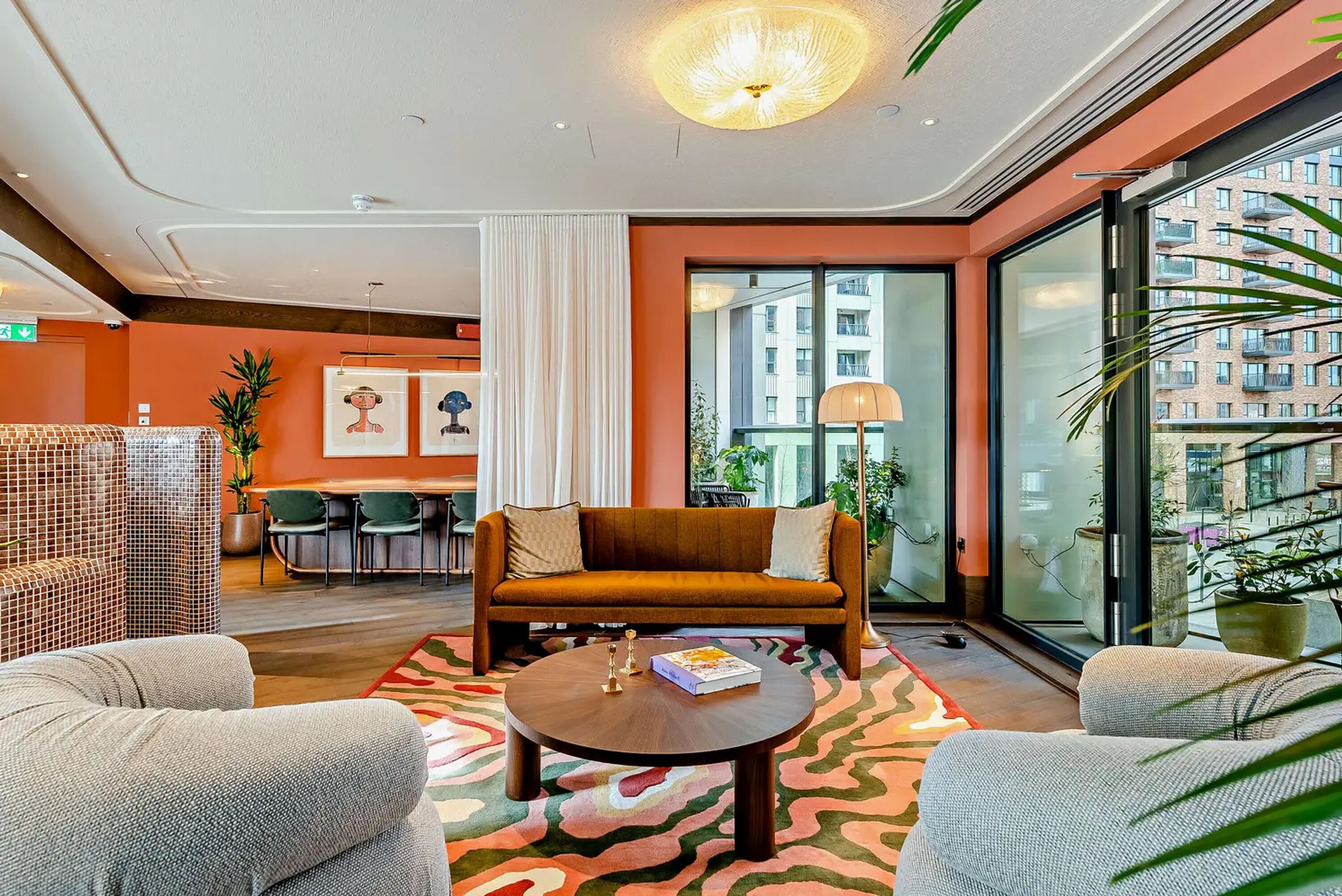 Un hall d’hôtel moderne avec un canapé, des fauteuils, une table ronde et une grande fenêtre donnant sur la ville.