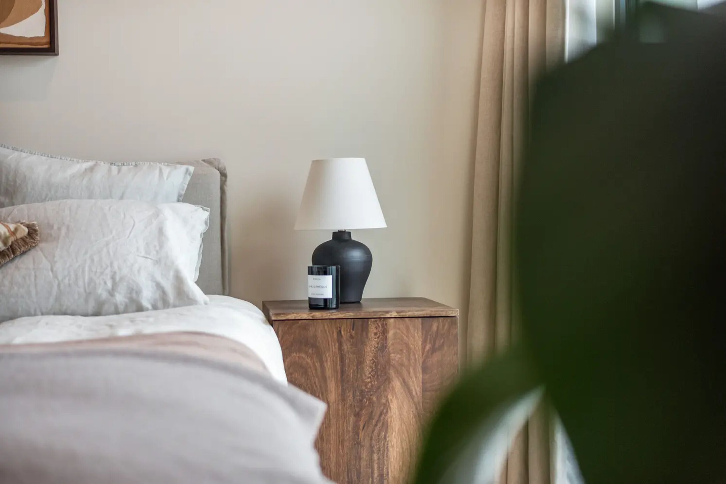 A neatly made bed with pillows, a bedside table with a lamp, and a framed picture on the wall.