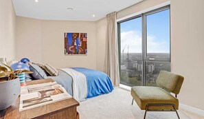 A modern bedroom with a large window, a bed, a chair, and a desk with a laptop. - Stylish Two-bedroom Flat With a Large Balcony (London)