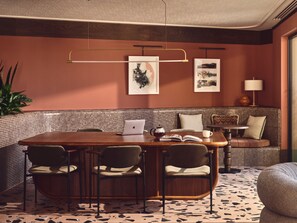A modern dining area with a wooden table, four chairs, a laptop, and a book. There are two framed artworks on the wall and a potted plant to the left. - Stylish Two-bedroom Flat With a Large Balcony (London)