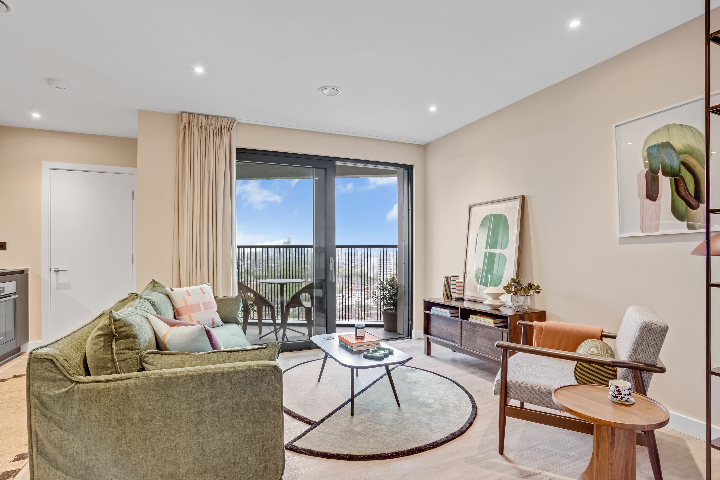 A modern living room with a sofa, coffee table, and chairs, a balcony with a view, and a kitchen area.