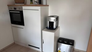 Ett kompakt kök med kylskåp, ugn, kaffebryggare och papperskorg.