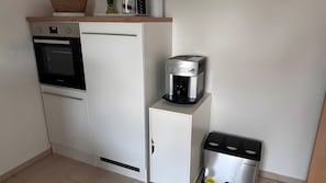 Una cocina compacta equipada con refrigerador, horno, cafetera y basurero.