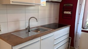 Ett kök med en diskho i rostfritt stål, en bänkskiva i trä, vita skåp och en röd vägg.