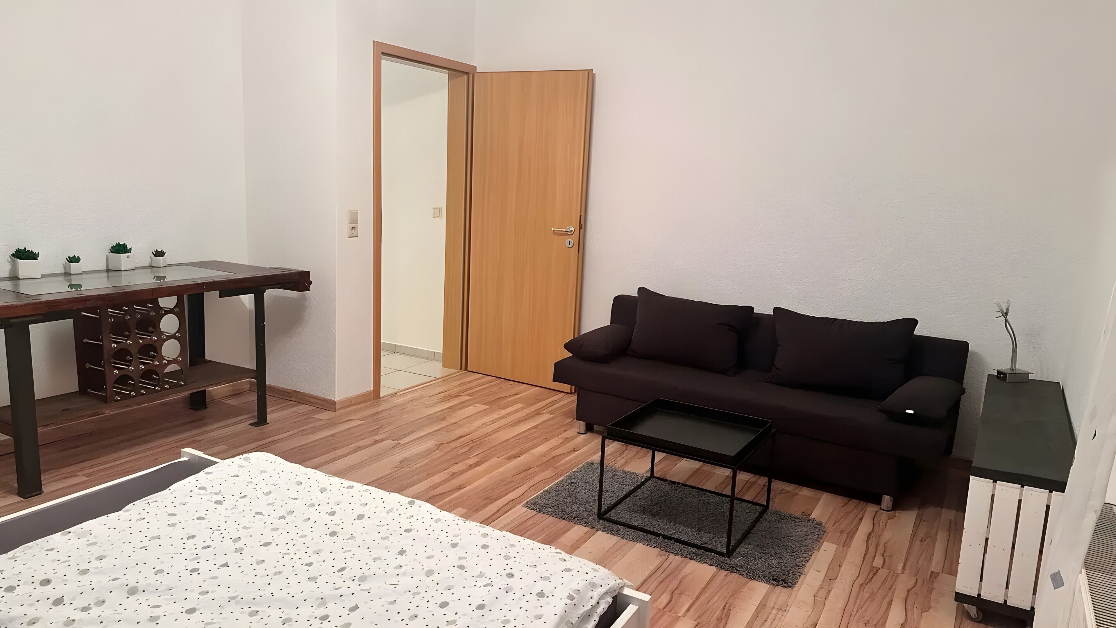 Une pièce comprenant un lit, un bureau en bois, un canapé sombre, une petite table et une porte.