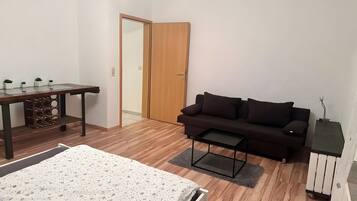 Une pièce comprenant un lit, un bureau en bois, un canapé sombre, une petite table et une porte.