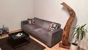 En grå soffa med blommiga kuddar, ett svart soffbord, en träskulptur och en krukväxt i en vit kruka.