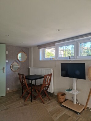 A room with a dining table, chairs, a television, a radiator, and windows with a view.