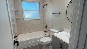 Un baño con bañera, inodoro y lavamanos, con un ventanal sobre el inodoro.