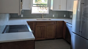 Una cocina con armarios blancos, un refrigerador de acero inoxidable, una ventana con vista a palmeras y un salpicadero de azulejos.