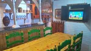 A dining area with a wooden table and green chairs, a television mounted on the wall, and shelves with various items.
