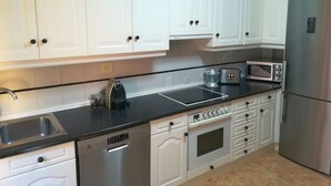 A modern kitchen with white cabinets, a stainless steel refrigerator, a microwave, a toaster, and a dishwasher.