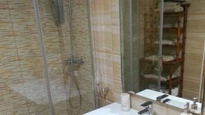 A bathroom with a glass shower enclosure, a white sink with a mirror, and a dark-colored vanity.