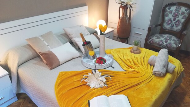 A neatly made bed with a yellow blanket, a book, a bottle, and a tray with fruit and a drink.