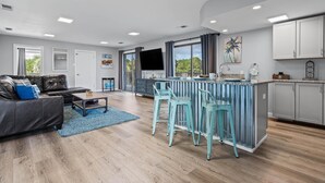 Una sala de estar moderna con sofá, mesa de centro y una zona de cocina con barra y taburetes de bar.