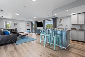 Ein modernes Wohnzimmer mit Sofa, Couchtisch und einer Küchenzeile mit Bar und Barhocker.