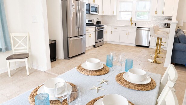 A modern kitchen with white cabinetry, stainless steel appliances, and a dining area set for a meal. - Cozy Wildwood House, Great Location, Private Parking, Walking distance to beach (Wildwood)