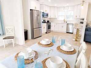A modern kitchen with white cabinetry, stainless steel appliances, and a dining area set for a meal. - Cozy Wildwood House, Great Location, Private Parking, Walking distance to beach (Wildwood)