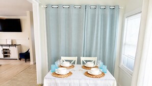 A dining area with a table set for four, a television mounted on the wall, and a kitchen area in the background. - Cozy Wildwood House, Great Location, Private Parking, Walking distance to beach (Wildwood)