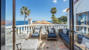 Un balcone con mobili in vimini, vista sul mare e palme.