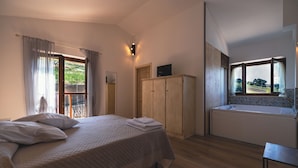 Quarto com cama, guarda-roupa de madeira, banheiro com banheira e varanda com cortinas.