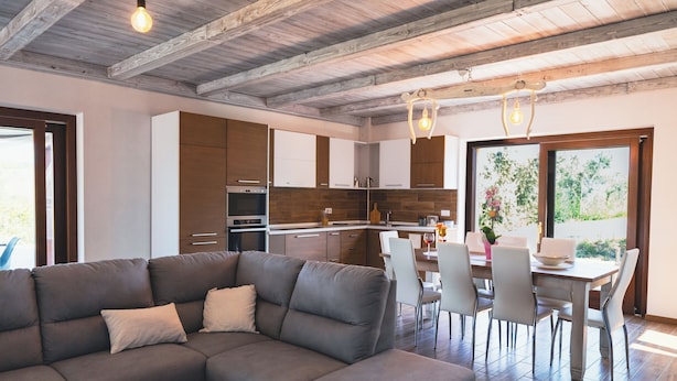 Cozinha moderna com armários de madeira, área de jantar com mesa e cadeiras, e um amplo sofá seccional.