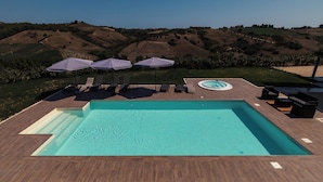 Piscina retangular com deck de madeira, rodeada por espreguiçadeiras e guarda-sóis, com vista para uma paisagem montanhosa.