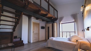 Quarto com escada de madeira, cama com edredom branco e mesa de cabeceira com abajur.