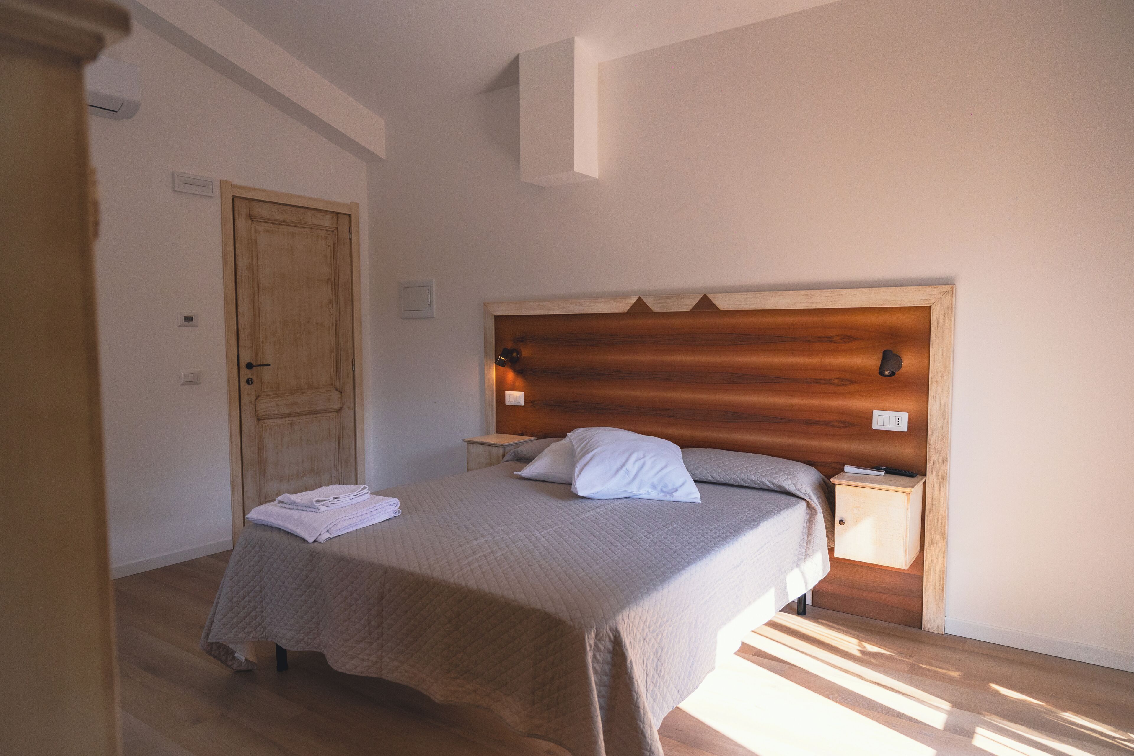 Ein Schlafzimmer mit einem hölzernen Kopfteil, einem Bett mit einer beigefarbenen Steudecke, zwei Nachttischen und einer Holztür.