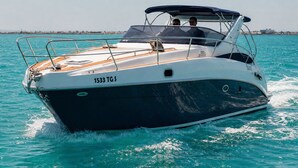 A speedboat with a cabin and two visible passengers, moving on clear turquoise water. - Dream boat (Tunis)