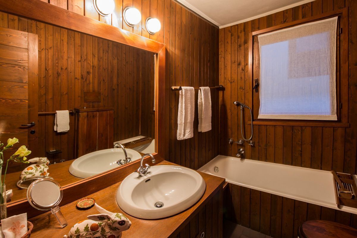 A wooden-paneled bathroom with two sinks, a large mirror, and a bathtub.