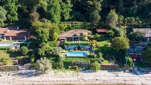 En stor bolig med swimmingpool, omgivet af frodig vegetation og en strand.