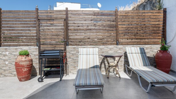 A patio with two sun loungers, a small table, and a large planter. - Casa Di Rena Country House: Panoramic Castle View & Endless Blue (Kritinia)