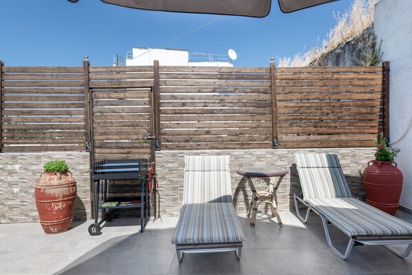 A patio with two sun loungers, a small table, and a large planter.