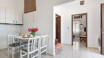 A clean, modern kitchen with white cabinetry, a dining table with chairs, and a small bench.