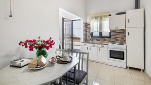 A modern kitchen with white cabinets, a stove, and a microwave. There's a dining table with chairs and a vase of flowers. - Casa Di Rena Country House: Panoramic Castle View & Endless Blue (Kritinia)